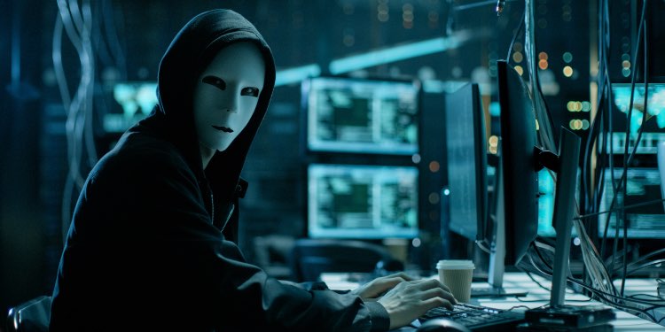 Hacker with white mask in a blue room full of computers