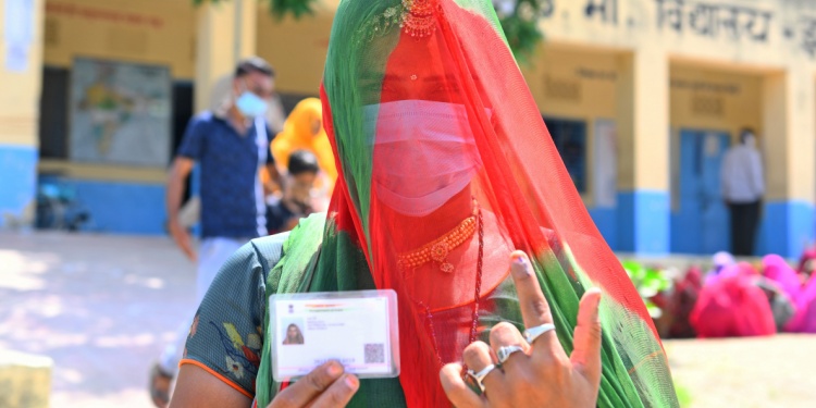 An Indian lady in a mask holding up a paper form of ID.