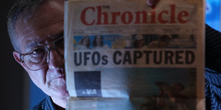 A man holding a UFO newspaper story.