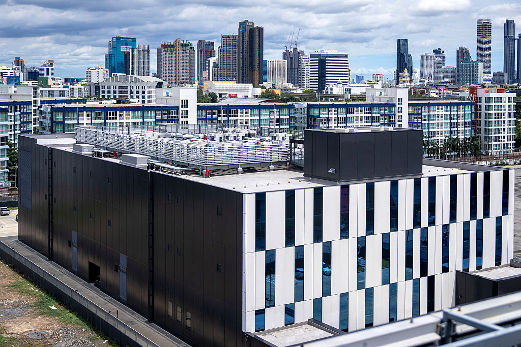 An aerial photograph taken from a nearby high-rise captures the Rama 9 data center facility situated directly within a densely populated residential community in Bangkok.