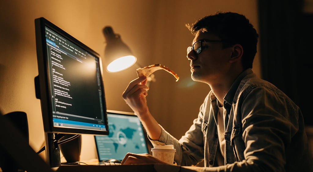 young programmer at home working and eating pizza