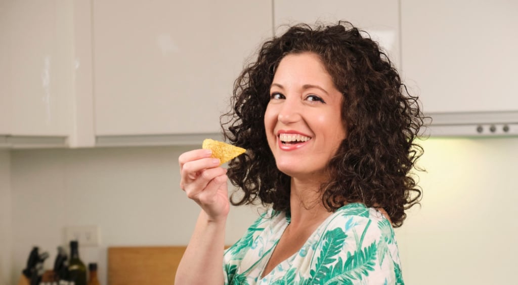 smiling woman with darl curly hairs holds a chip, wear a green and white blouse