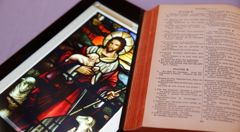 stained glass window with jesus and a sheep and an open bible