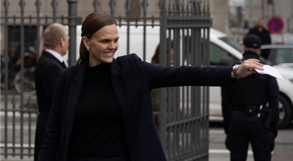 female brunette in black jacket and top with her left hand holding a paper