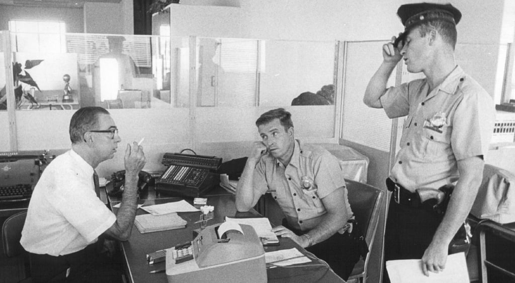 Black and white photo of office workers and a cop.