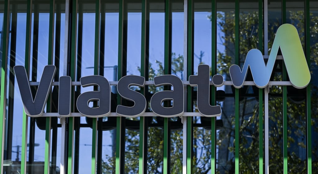 viasat black sign on glass wall reflecting blue sjy and trees