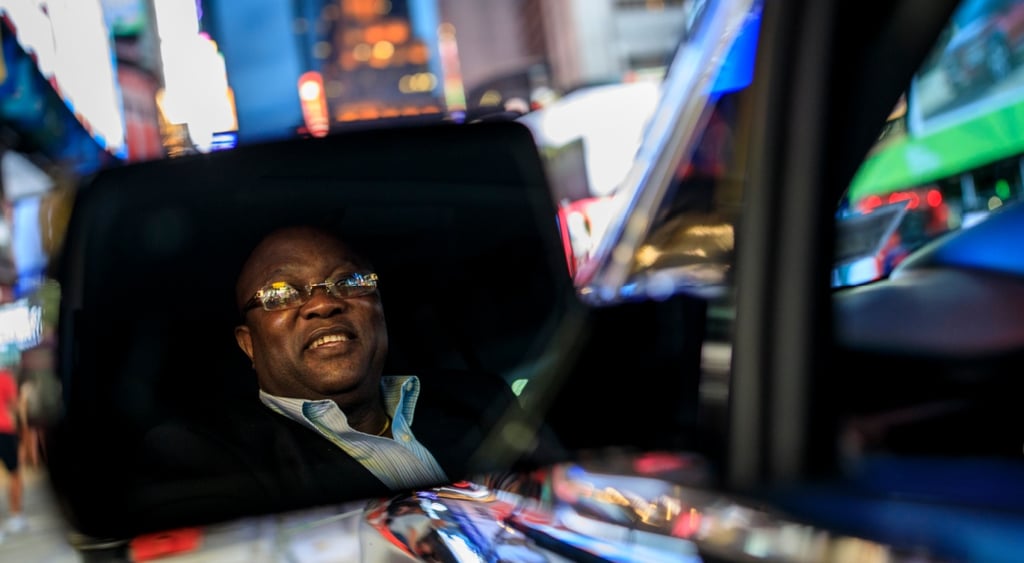 An uber driver, in the city, seeing himself in the wing-mirror.