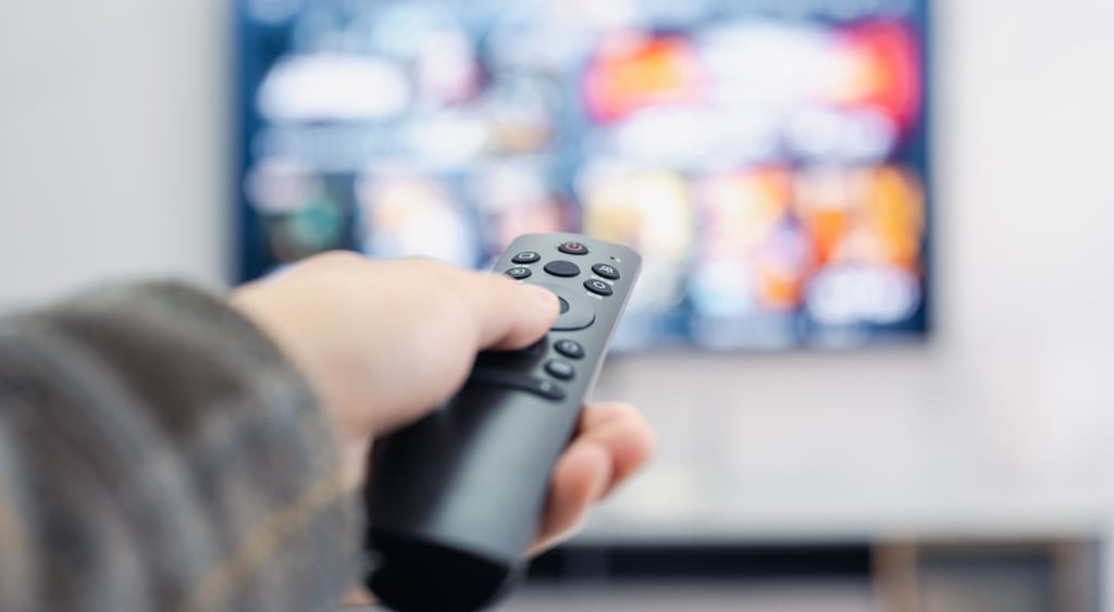 black remote control in white hand, pointing to a colorful television