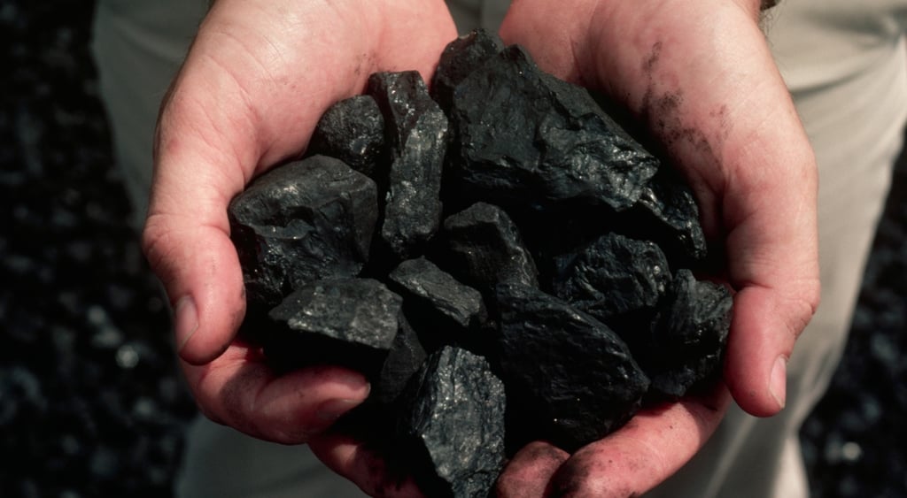 dirty white man's hands hold small coal pieces
