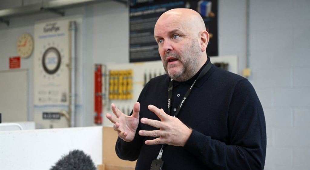 bald man, black turtleneck, mild beard, white wall, yellow clock, dead cat mic
