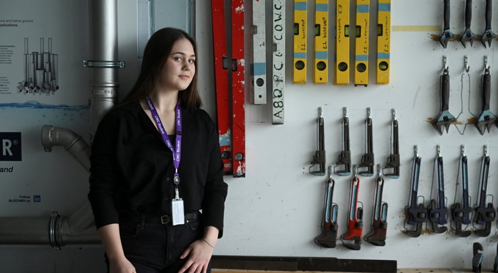 young woman, brown hair, plumbingtools, purple strap with white card, silver pipe