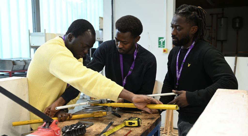 three black men, black sweaters, yellow sweater, two yellow pipes, measurements, plumbing