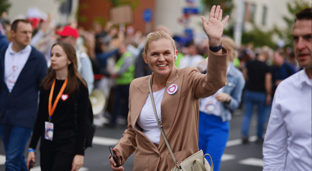 Barbara Nowacka, white woman in sand color jacket and throusers waves hand