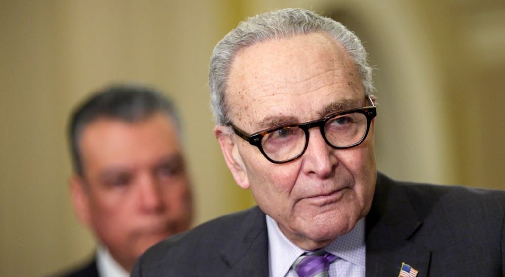 Chuck Schumer, grey hair, black frame glasses, grey hair, white collar, black suit,
