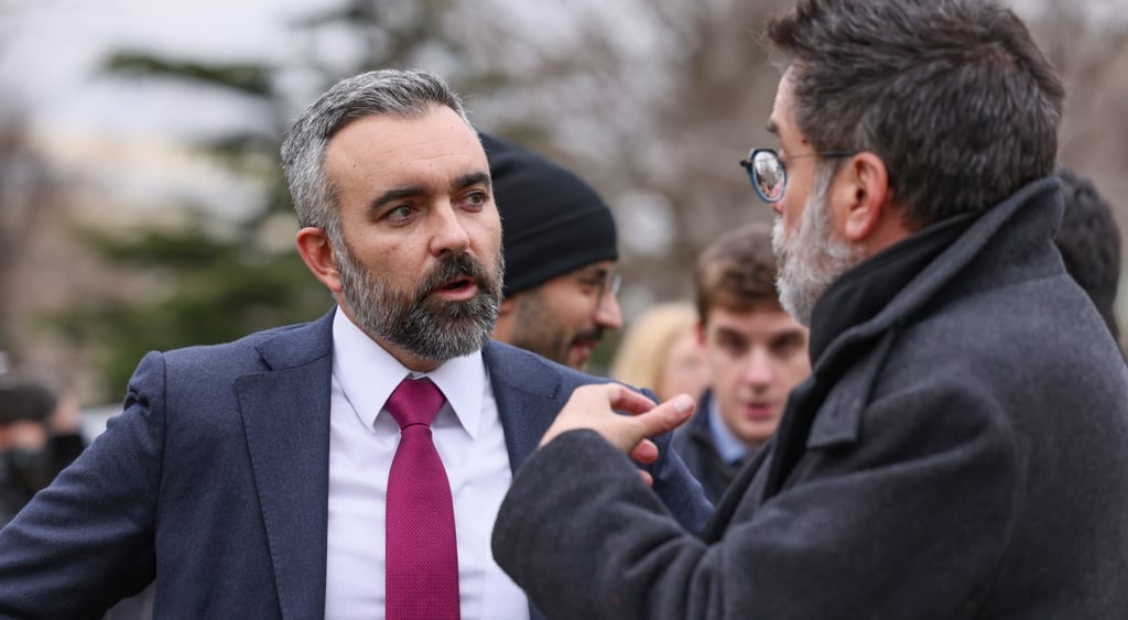 Raul torrez, man, grey har, dark bead, bordo tie, white shirt, talks to man in dark grey suit