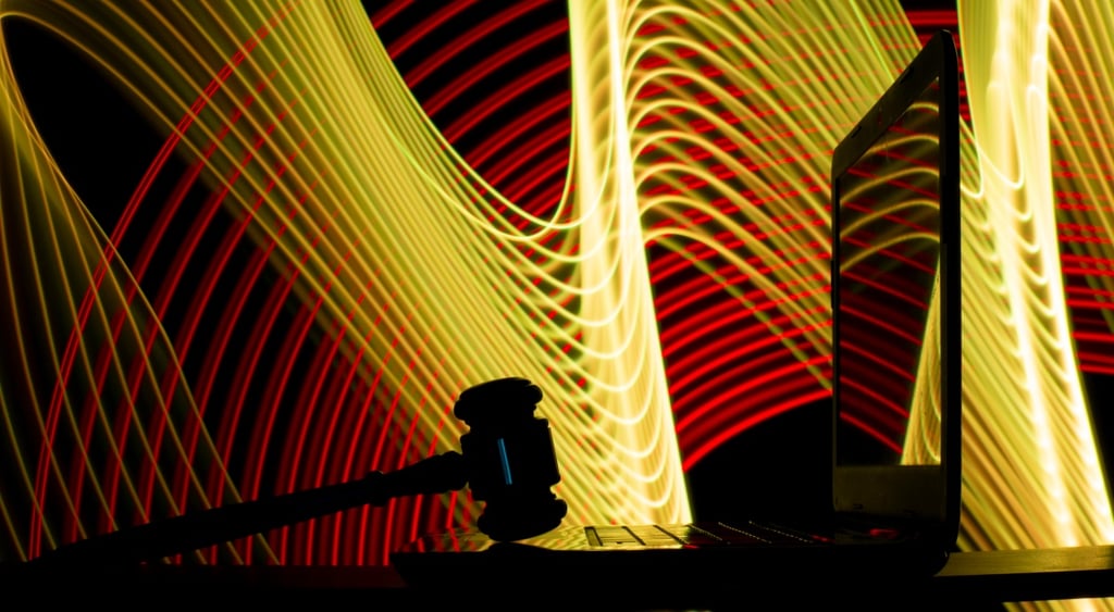 black court gavel, black laptop, screen reflects yellow, brown light painting