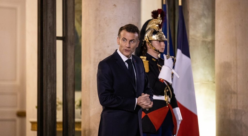 emmanuel macron hold his hands together, secuirity guard in uniform, french flag in the back