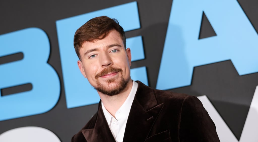 mr beast, black suit, white shirt, photo wall with big blue letters, black background