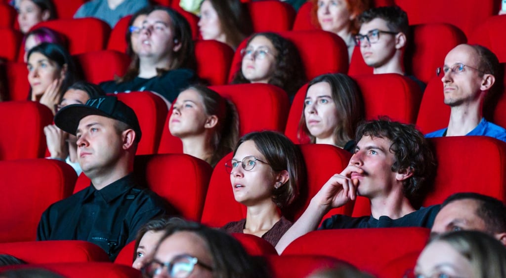 people in red cinema chairs looking at the big screen, well lit