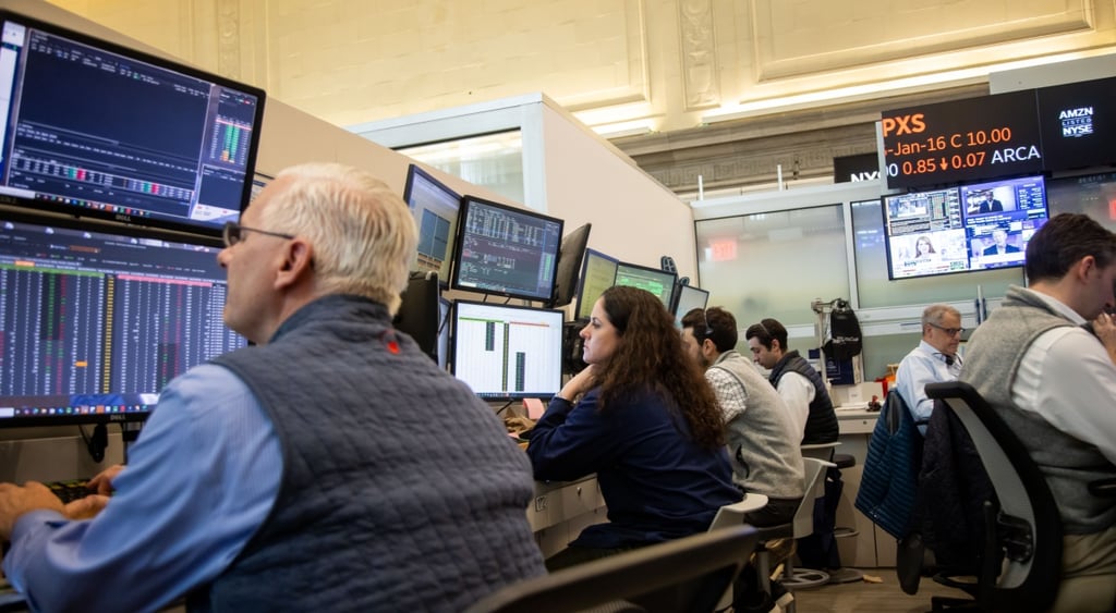 people in front of screens with trade numbers, old man in grey west, grey hair, blue shirt