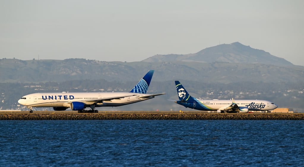 alaska airlines plane takes off, united airlines plane lands, dark water, blue sky, brown mountains