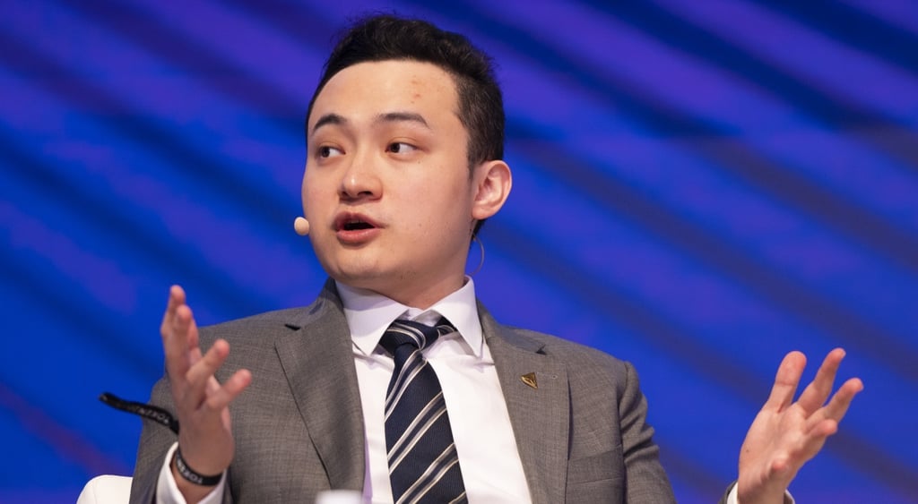 justin sun, white asian man, grey jacket, white collat shirt, dark blue tie with white stripes,