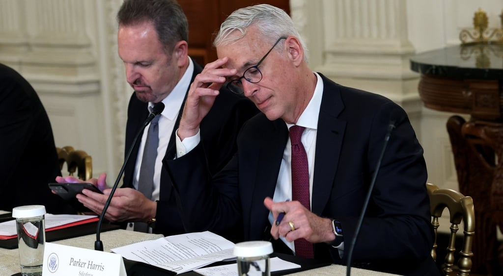 Parker Harris in meeting, black suit, bordo tie, white collar shirt, grey hear, facepalm