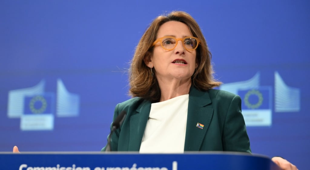 Teresa Ribera, EU-blue photo wall, green jacket, white shirt, darker blue podium, light brown hair