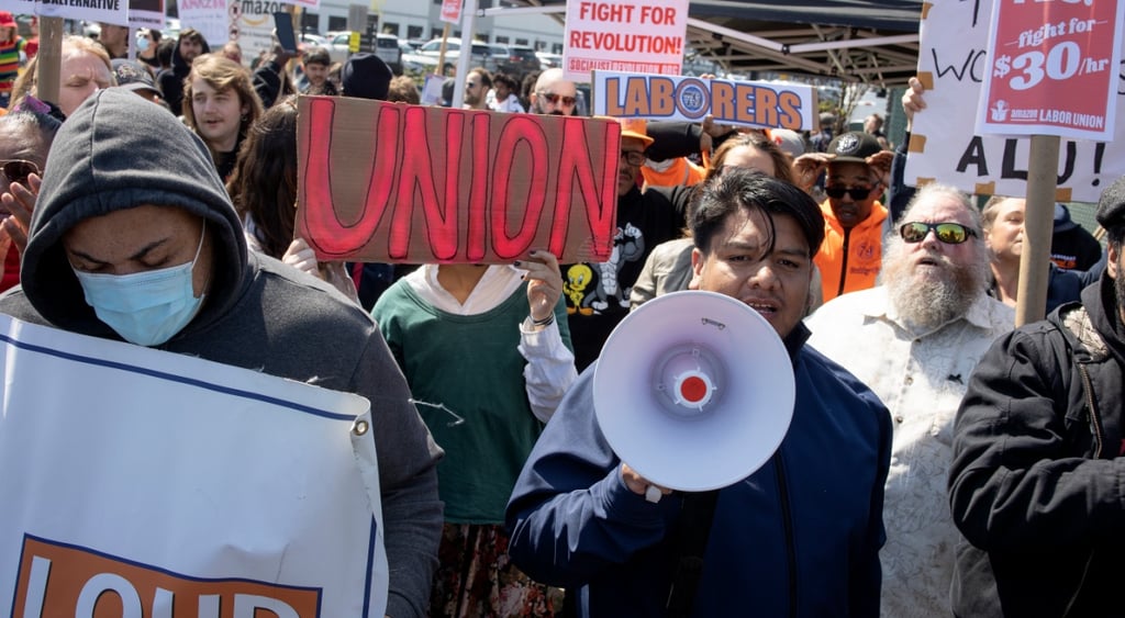 rally, white megaphone, people holding up white signs, red letters, union, black jacket, face mask