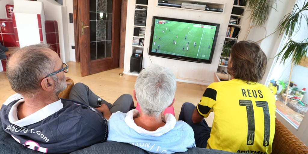 family of three wantches european futbool on tv, black frame, green grass field, yellow shirt