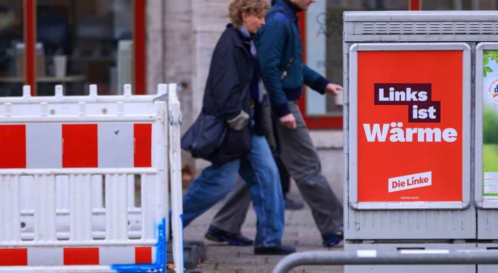 red poster on sidewalk, grey frame, to pedestrians walking by, black leather jacket, die linke
