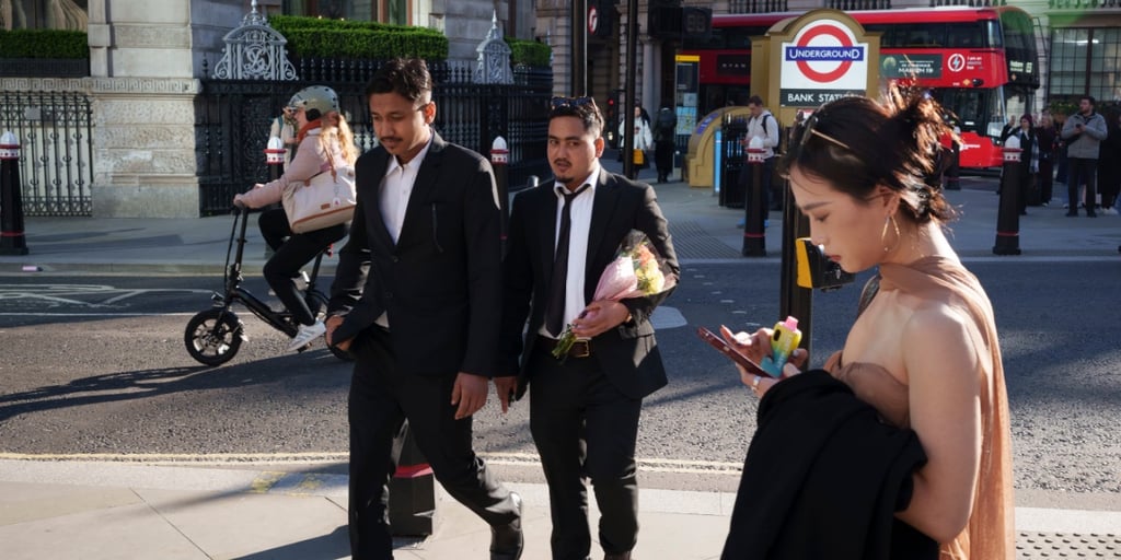 Weiße asiatische Frau, ärmelloses Oberteil, zwei dunkel gekleidete asiatische Männer in schwarzen Anzügen, Londoner U-Bahn, sonnig