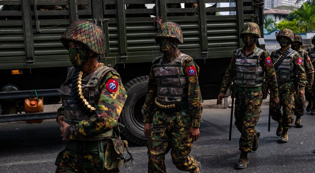 four myanmar army men stand guard in helmets, faces covered, uniforms, red badges