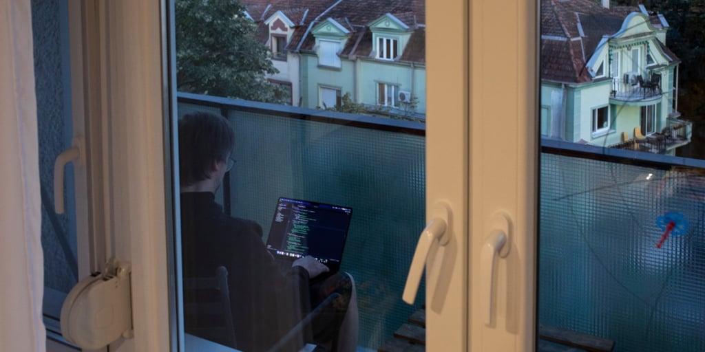 man in balcony, working on laptop, light brown wood door frame, code, old building outside