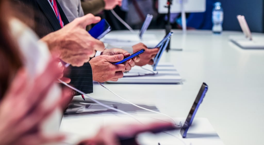 seven samsung galaxy phones, held in human hands or placed on white desk in tech event