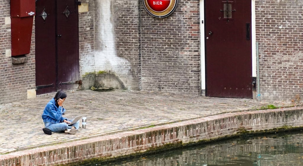 woman, dutch canal, water, light brown-greyish bricks, blue jeans, blue jacket, black hair
