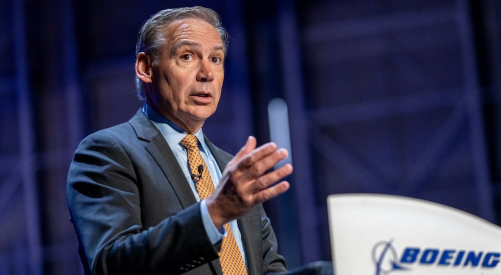 Kelly Ortberg, dark blue suit, orange and blue tie, raised left arm, grey hair, white man, tan