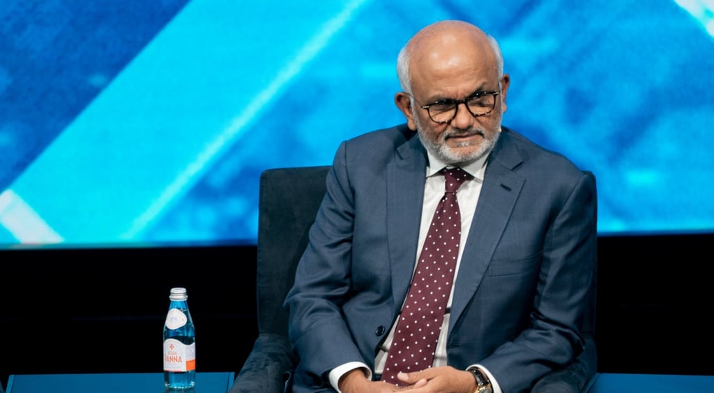 Shantanu Narayen, old chubby indian man sits, dark blue suit, bordo tie, white shirt, bald, glasses