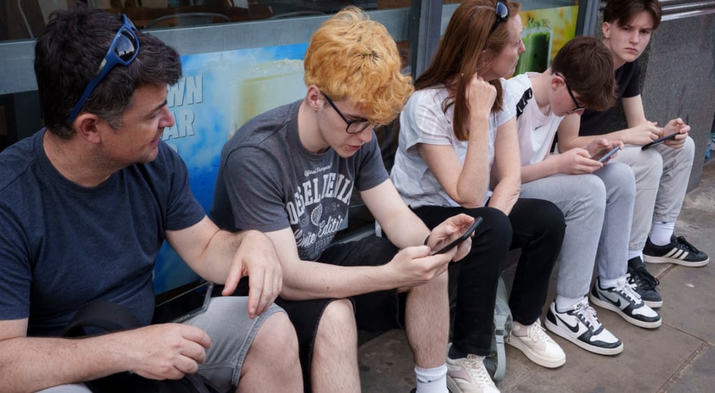 yellow curly hair, young white teen, grey tshirt, smartphone, three other people, glasses