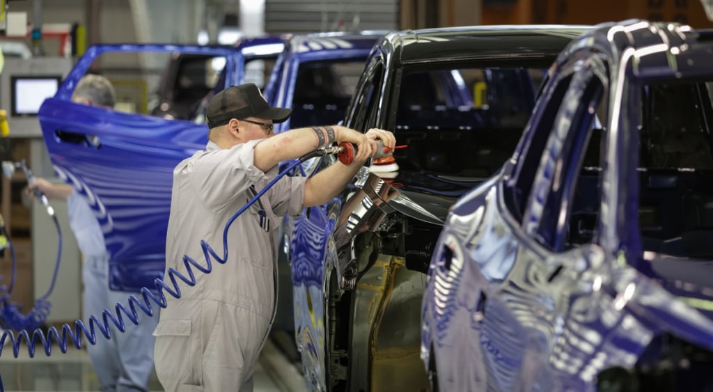 Volkswagen workers, dark blue and black EVs, ligt grey jumpsuit, short sleeves, black hat,