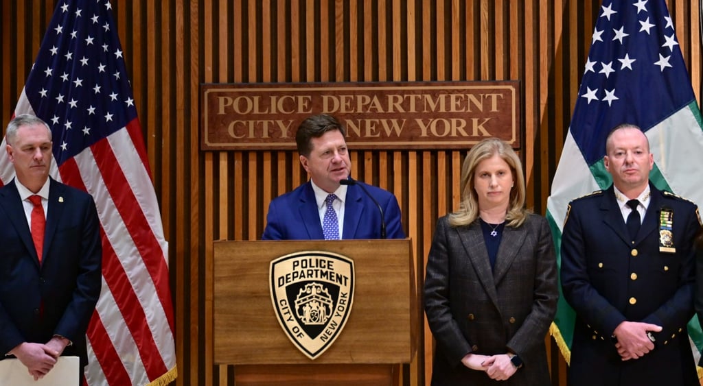 jay clayton, dark blue suit, two usa flags, two men in black suits, red tie, black tie, blonde woman
