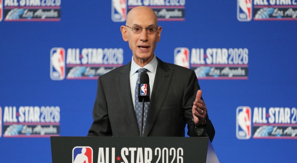 adam silver, nba blue photo wall, tall bald man, glasses, dark grey suit, white collar shirt, mic