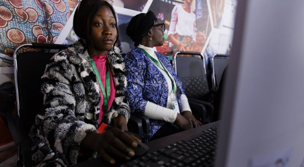 black woman on grey laptop, pink blouse, black leather seat, black woman in white and blue top