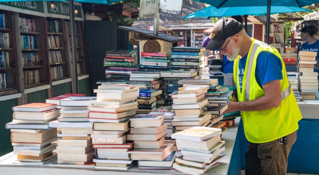 old man, live yellow reflective vest, blue tshirt, piles of books, shelves of books, tan, brown shorts