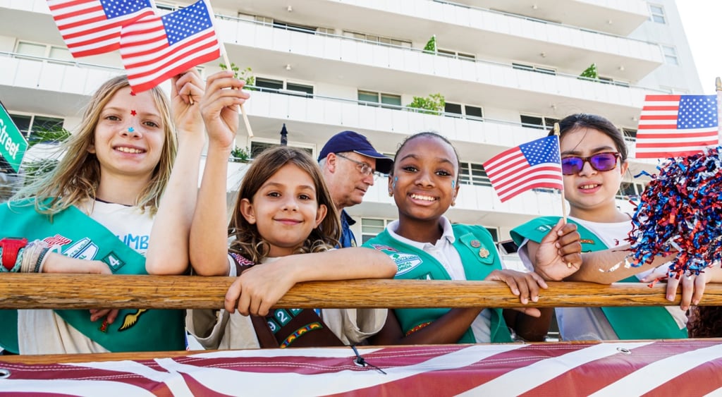 girl scouts and Brownies, white blonde girl, US flag, young black girl, white apartment building