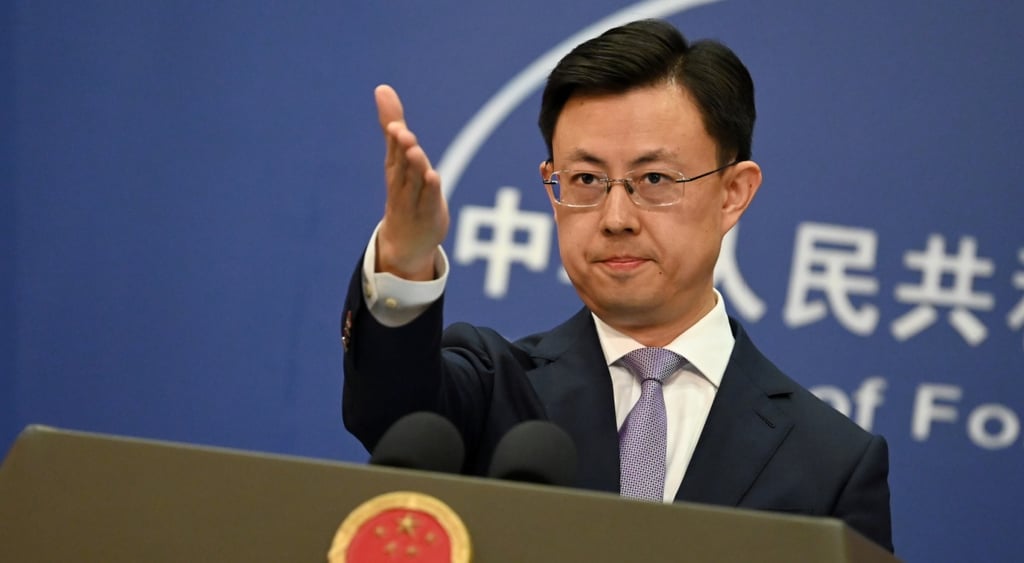 young asian man, tanned, hand up, black suit, grey tie, black hair, white shirt, dark blue photowall