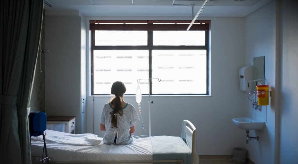 grey-blueish hospital room, big window, woman sitting on bed, ponytail, curtains, white sheets