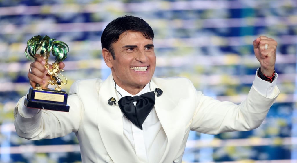 Sal Da Vinci, white suit, black hair, golden statue prize in hand, wide white smile, black hair