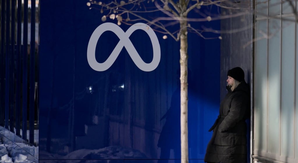 dark grey meta logo on dark blue wall, winter, woman in long black winter coat, blonde,
