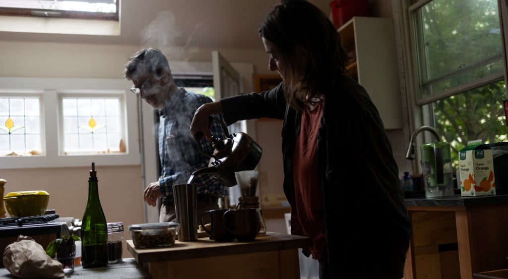 early morning, kitchen man and woman, woman pours coffee, green trees, stream red blouse